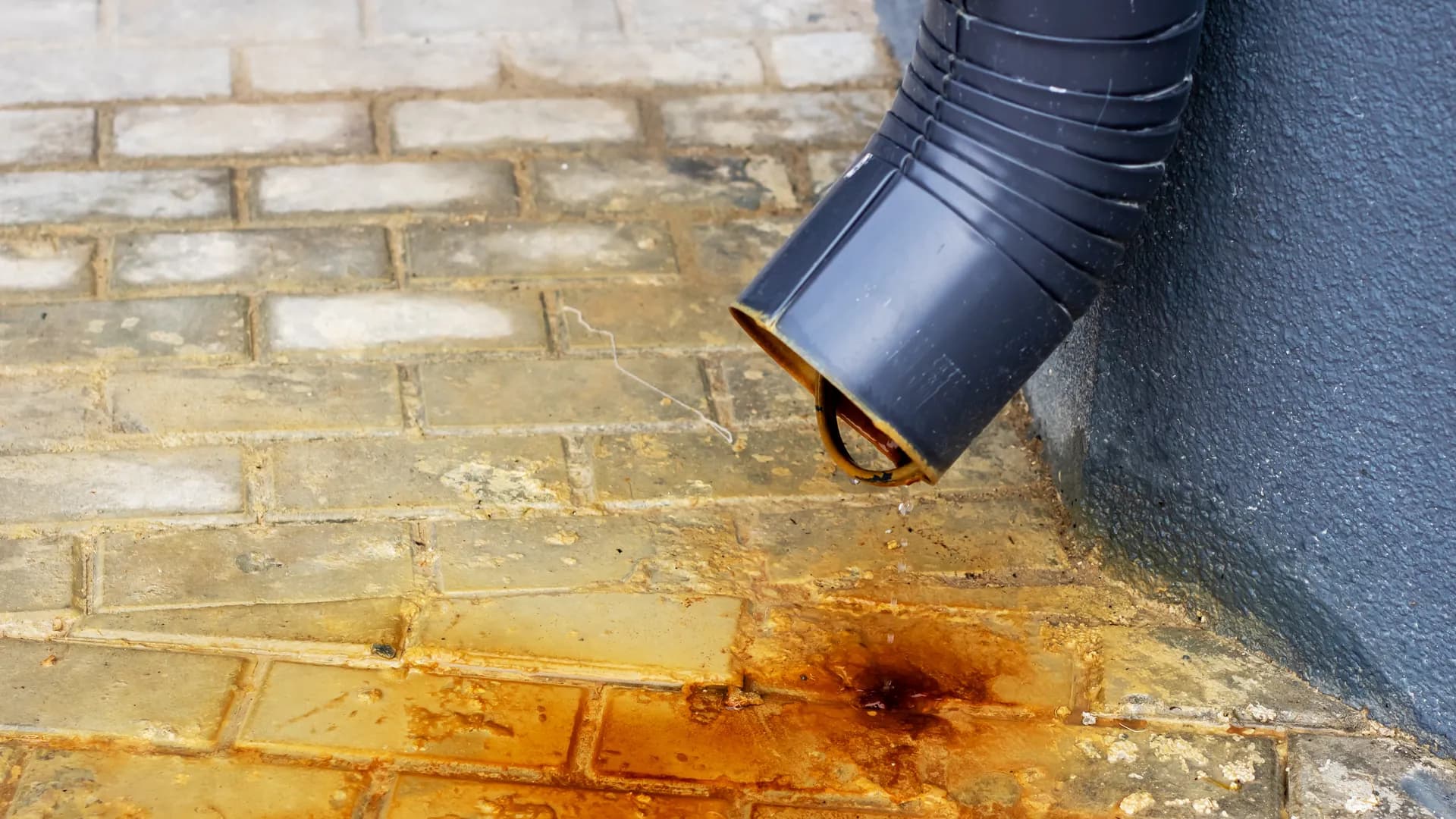 Rust staining on a brick path beneath a downspout